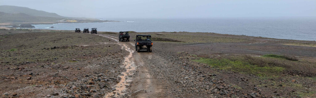 A line of UTVs driving along a rugged coastal trail