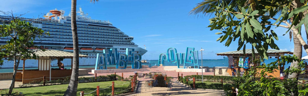 A large cruise ship docked behind a colorful Amber Cove sign