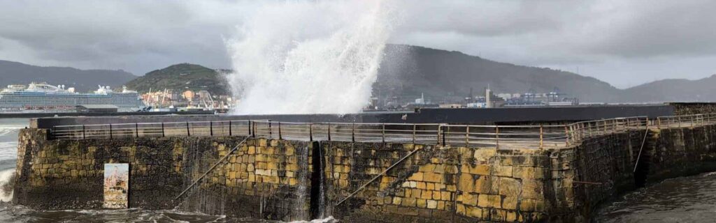 Waves crashing against a stone pier with a cruise ship in the background
