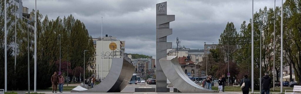 Monument to the Polish Sailor framed by trees and storm clouds near Kościuszko Square in Gdynia.