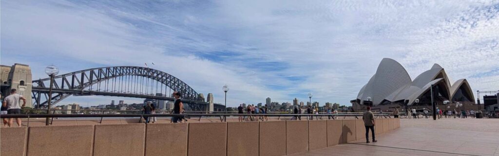 The Sydney Harbour Bridge and Sydney Opera House frame a panoramic waterfront view beneath streaked clouds.